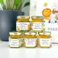 Jars of honey with personalized labels on a white surface, with a blurred background.