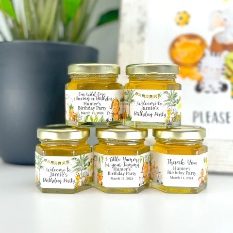 Jars of honey with personalized labels on a white surface, with a blurred background.