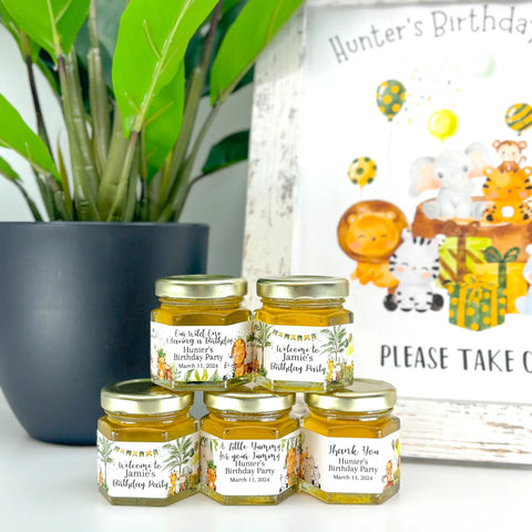 Jars of honey with personalized labels on a table next to a children's birthday party sign.