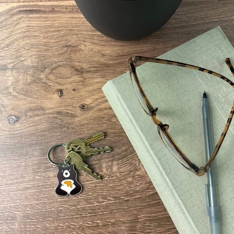 Keys with a bear keychain, glasses, and pen on a book on a wooden surface