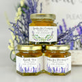 Three jars of honey stacked on a white surface with lavender flowers in the background
