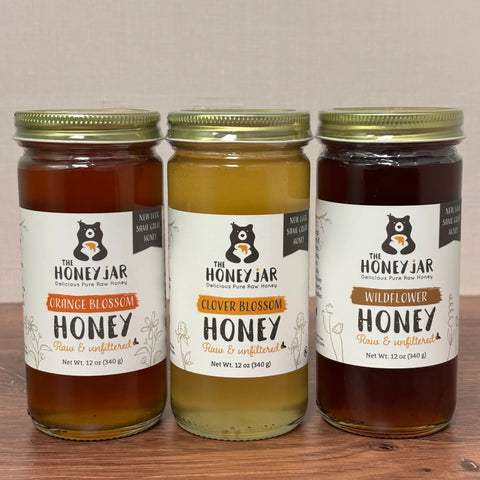 Three jars of honey from The Honey Jar on a wooden surface with a neutral background