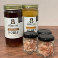 Two jars of honey and two small containers of salt on a wooden surface.