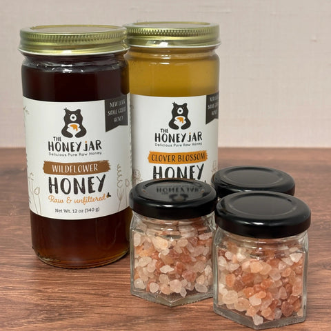 Two jars of honey and two small containers of salt on a wooden surface.