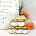 Jars of honey with personalized labels on a table with flowers in the background