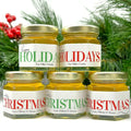 Five jars of honey with personalized holiday labels against a green foliage background