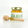 Jar of honey with a gold lid and wooden honey dipper on a white background