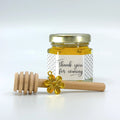 Jar of honey with a gold lid and wooden dipper on a white background