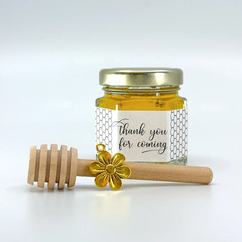 Jar of honey with a gold lid and wooden dipper on a white background