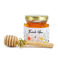 Jar of honey with a floral label and wooden honey dipper on a white background