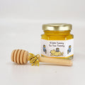 Jar of honey with a wooden dipper and gold bee charm on a white background