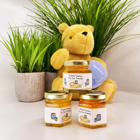 Yellow teddy bear with honey jars on a white surface with plants in the background