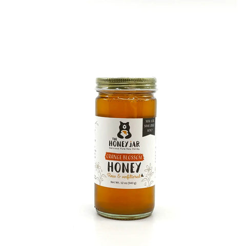 Jar of orange blossom honey with a label on a white background