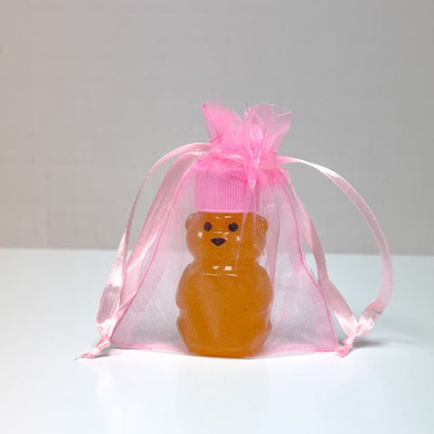 Small bear-shaped bottle with a pink cap inside a transparent pink organza bag on a white background