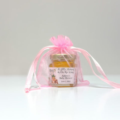 Jar of honey in a pink organza bag with a personalized label on a white background
