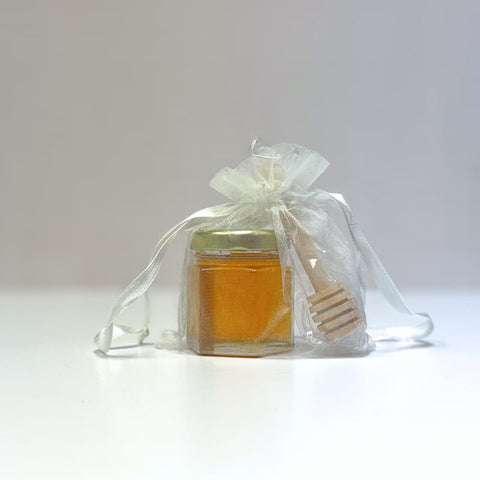 Jar of honey with a honey dipper inside a transparent white drawstring bag on a white background