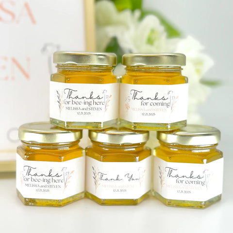 Five small jars of honey with personalized labels on a white background