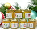 Jars of honey with Christmas-themed labels on a white background with holiday decorations.