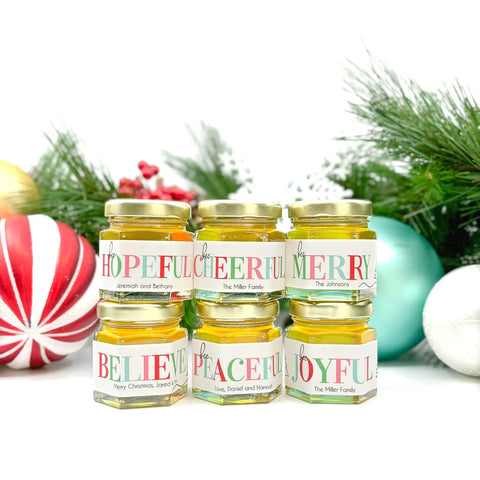 Jars of honey with Christmas-themed labels surrounded by festive ornaments on a white background