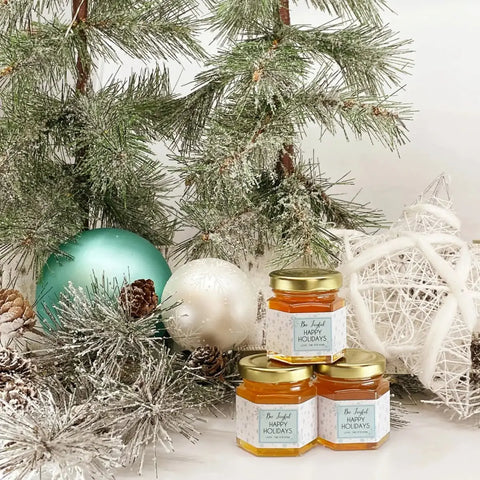 Jars of honey under a decorated Christmas tree with ornaments and lights.