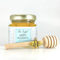 Jar of honey with a gold lid and a honey dipper on a white background