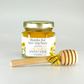 Jar of honey with a personalized label and a wooden honey dipper on a light background