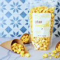 Bag of Utah Honey Corn popcorn with cones and scattered popcorn on a patterned background