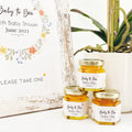 Jars of honey with personalized labels on a white surface with a plant in the background.