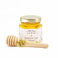 Jar of honey with a gold lid and wooden dipper on a white background