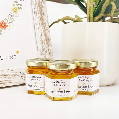 Three jars of honey with gold lids and personalized labels on a white surface