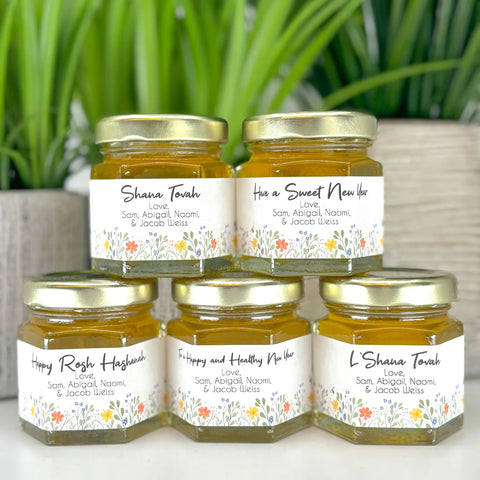 Five jars of honey stacked on a white surface with decorative labels.