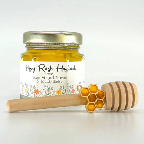 Jar of honey with a decorative label and wooden honey dipper on a white background