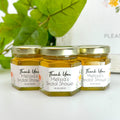 Three jars of honey with personalized labels on a white surface.