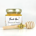 Jar of honey with a personalized label and a wooden honey dipper on a white background