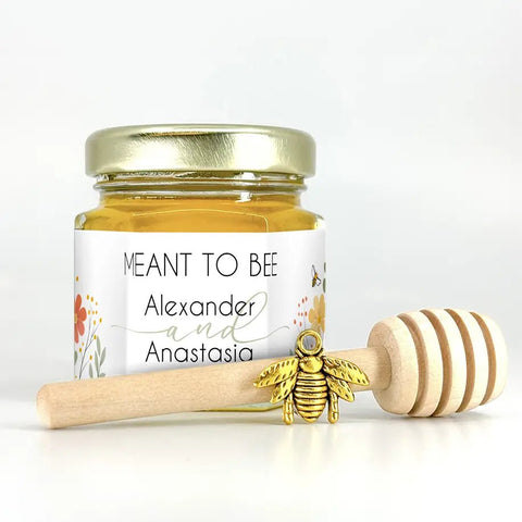 Jar of honey with a gold lid, gold bee charm, and wooden dipper on a white background