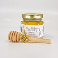 Jar of honey with a personalized label and wooden honey dipper on a white background