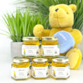 Jars of baby food with personalized labels, and a teddy bear on a white surface with greenery in the background.