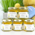 Five small jars with personalized labels on a white surface, with a blurred background.
