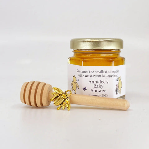 Jar of honey with a wooden dipper and bee charm on a white background