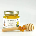 Jar of honey with a personalized label, wooden honey dipper, and honeycomb charm on a white background
