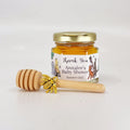 Jar of honey with a gold lid, gold bee charm, and wooden honey dipper on a white background