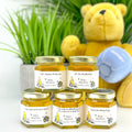 Jars of honey with personalized labels in front of a teddy bear and plant