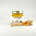 Jar of honey with a wooden dipper and honeycomb charm on a white background