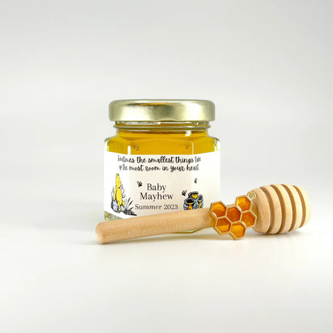 Jar of honey with a wooden dipper and honeycomb charm on a white background