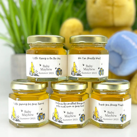 Five jars of honey with personalized labels on a white surface, with a blurred background.