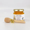 Jar of honey with a wooden honey dipper and gold bee charm on a white background