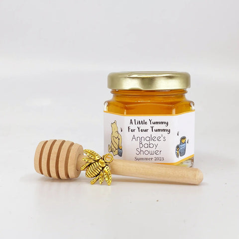 Jar of honey with a wooden honey dipper and gold bee charm on a white background