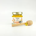 Jar of honey with a wooden dipper and baby feet charm on a white background