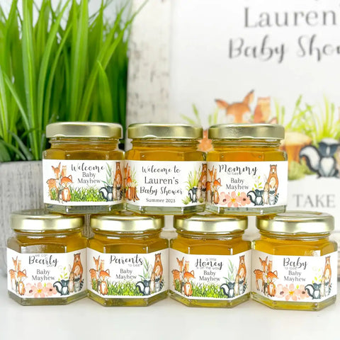 Jars of honey with personalized labels for a baby shower on a white surface.