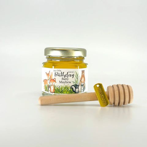 Jar of honey with a personalized label and wooden honey dipper and gold thank you charm on a white background